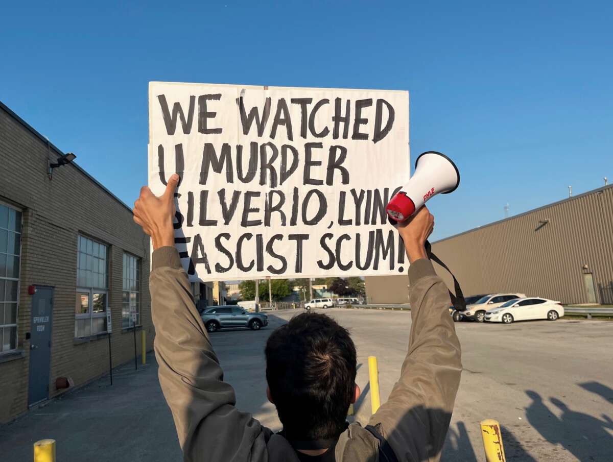 Un manifestant détient un panneau qui lit "Nous vous regardons assassiner Silverio qui mente une écume fasciste."