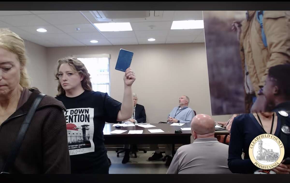 Bobbi Erickson, de la Shut Down Detention Coalition, tourne le dos aux commissaires du comté de Clearfield qui refusent de la laisser, ainsi que d'autres personnes de l'extérieur du comté, s'exprimer lors de la partie de commentaires publics d'une réunion du 26 mai sur les raisons pour lesquelles ils devraient voter en faveur de l'annulation de leur contrat avec ICE et GEO Group pour le centre de traitement de Moshannon Valley.